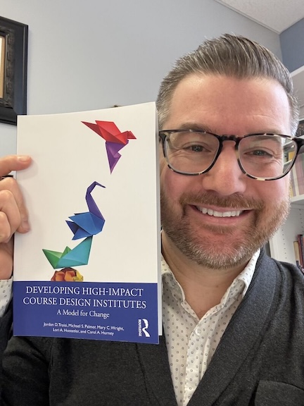 Jordan T. holds a copy of his book "Developing High-Impact Course Design Institutes: A Model for Change!"