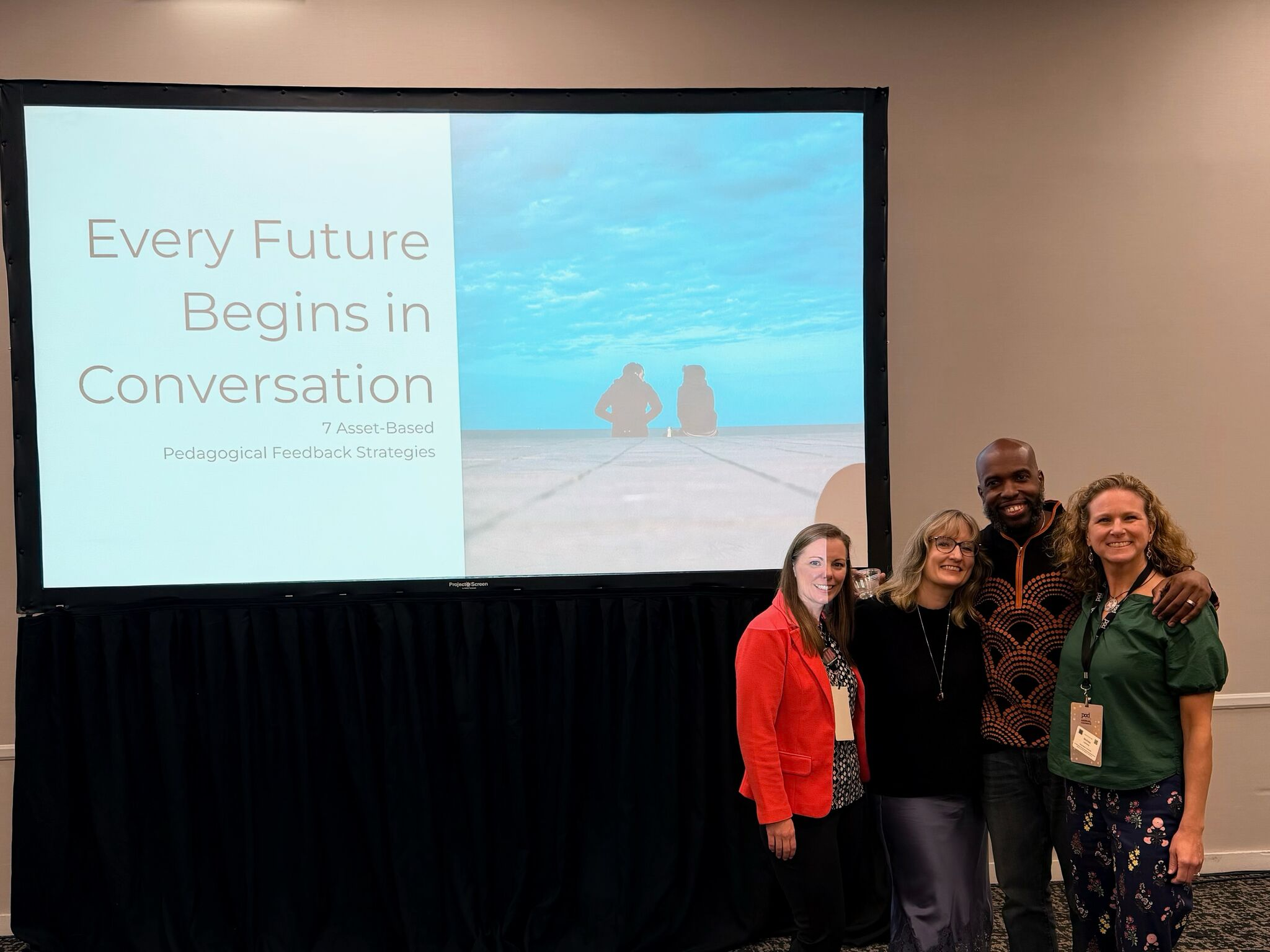 Four educational developers smile at the camera in front of a title slide "Every Future Begins in Conversation"